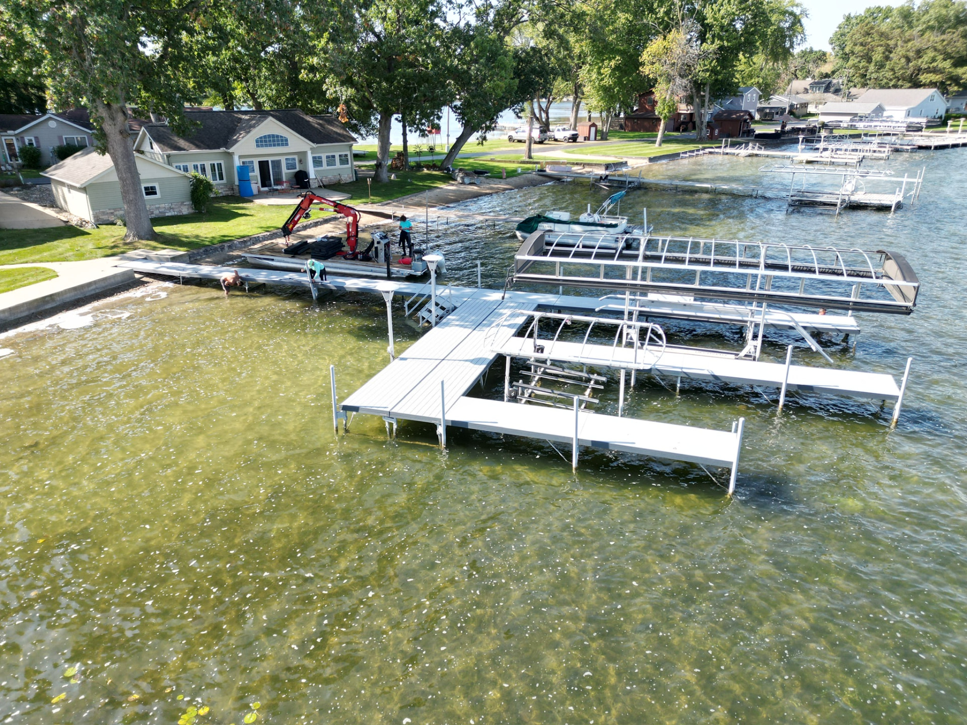 Beach Bumz dock and boat lift installation underway on a Michigan lakefront, with a crane barge at the shoreline