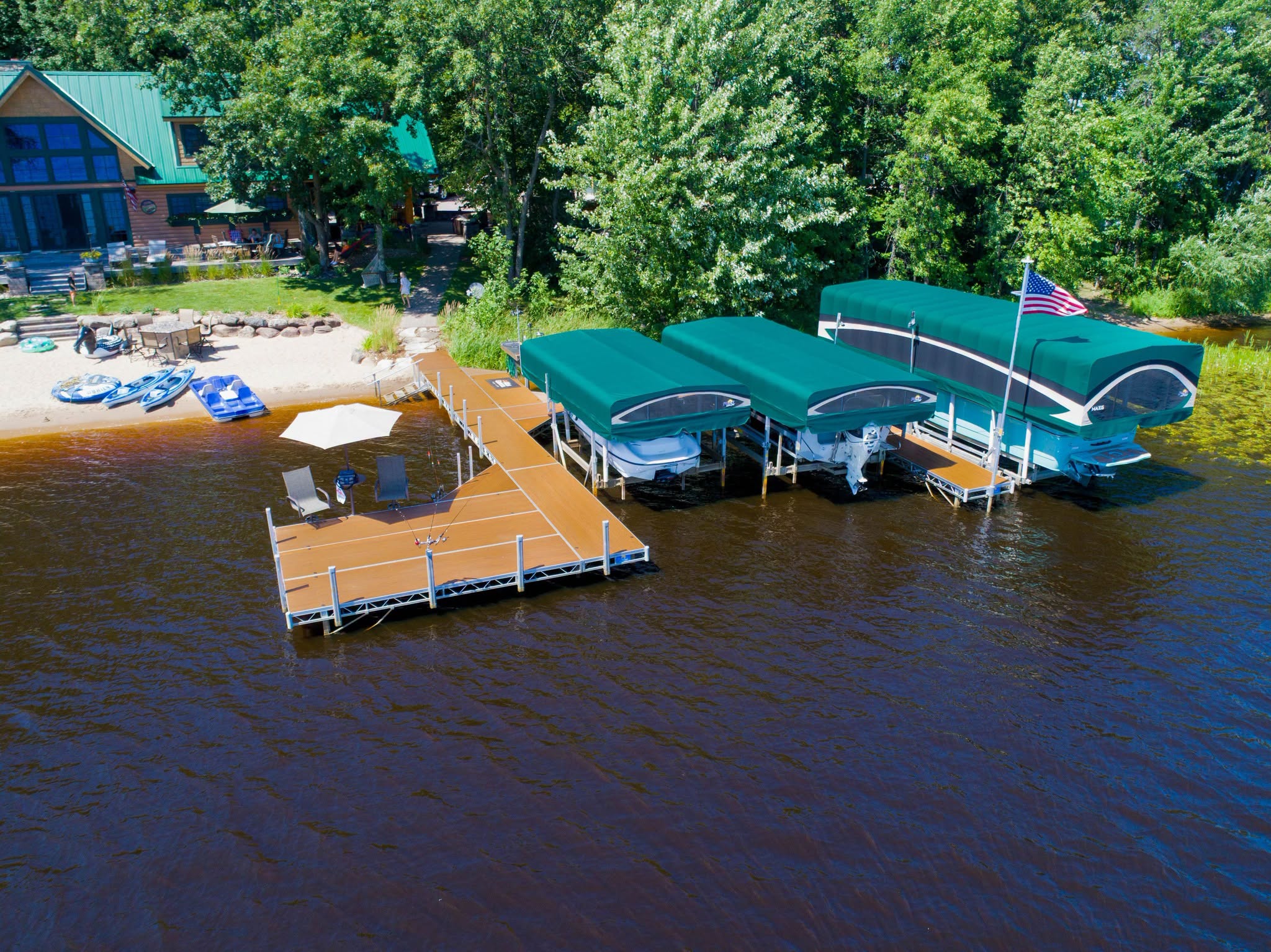 Pontoon and tritoon boats raised on covered lifts beside an aluminum lake dock
