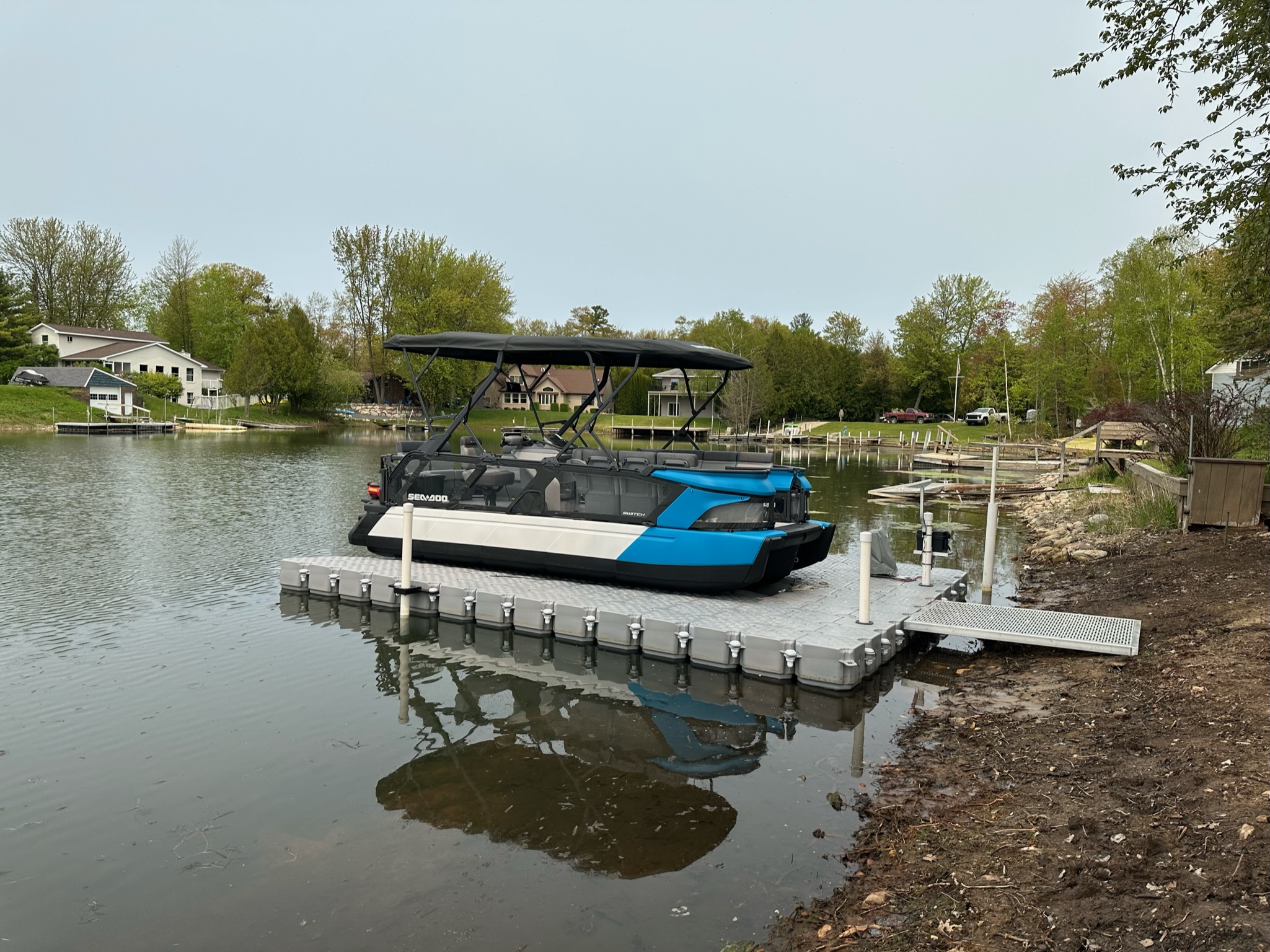 Sea-Doo Switch supported above the water on a CanDock drive-on system beside a residential shoreline