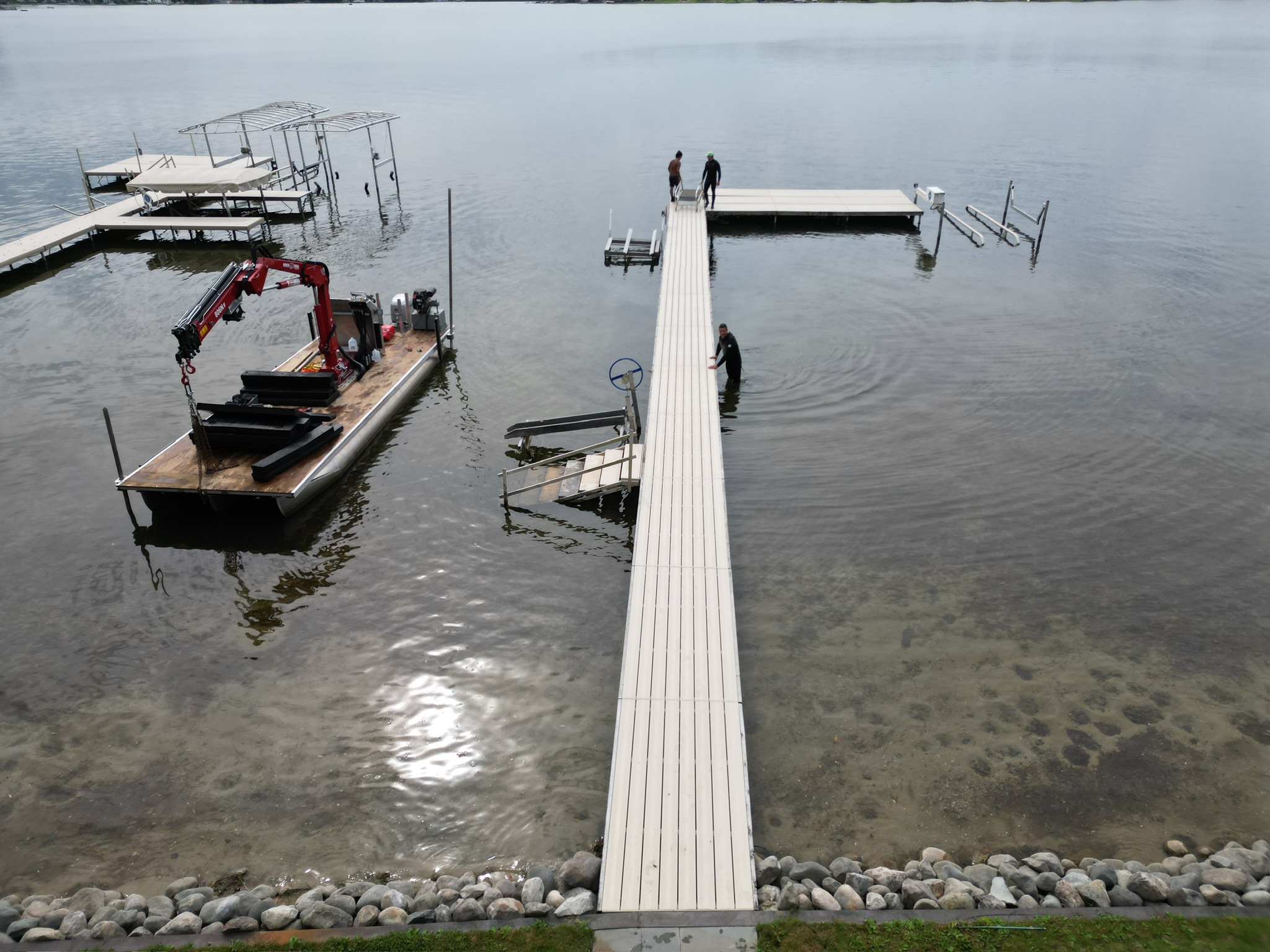 Long white dock walkway extending into a calm Michigan lake with a work barge and boat lifts nearby