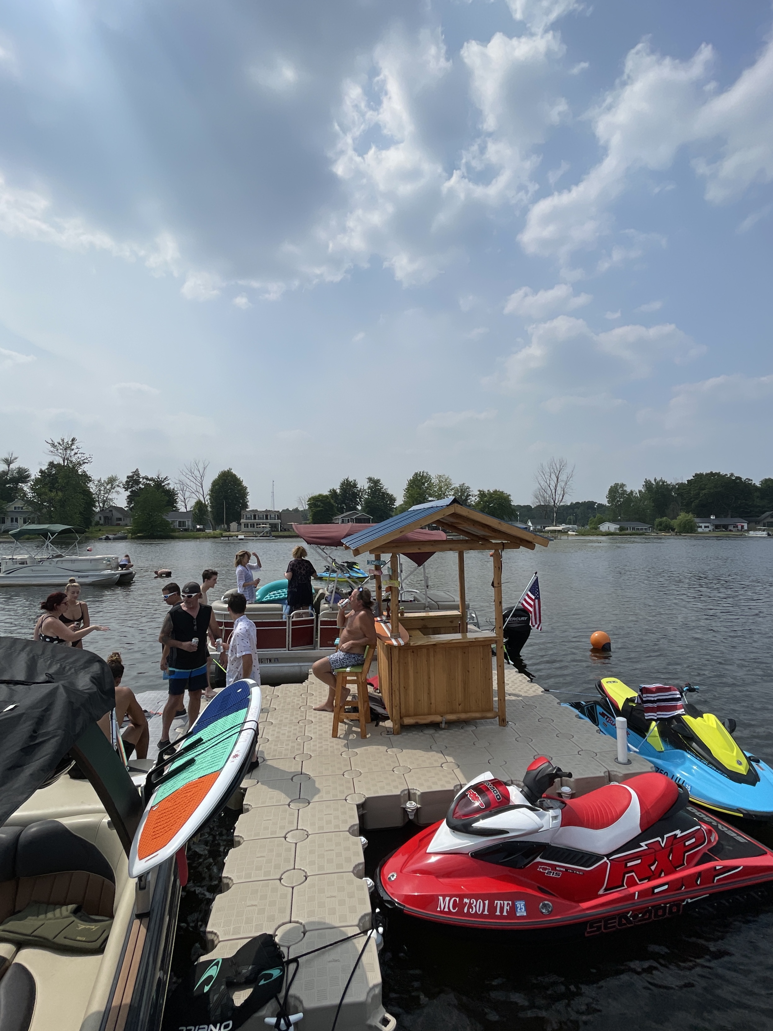 Friends gathered on a floating dock with personal watercraft tied alongside on a Michigan lake