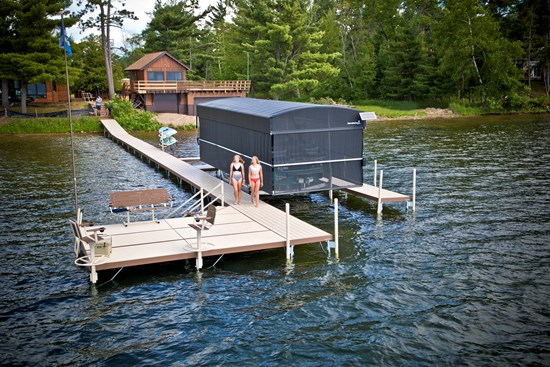 ShoreStation sectional dock with a dark canopy enclosure at the end of a long walkway on a wooded lake
