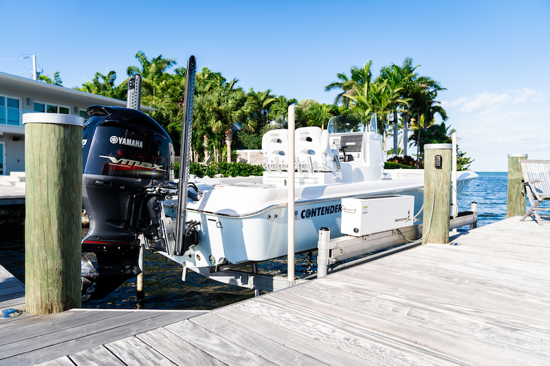 Center-console fishing boat raised on a pile-mounted boat lift alongside a wood dock